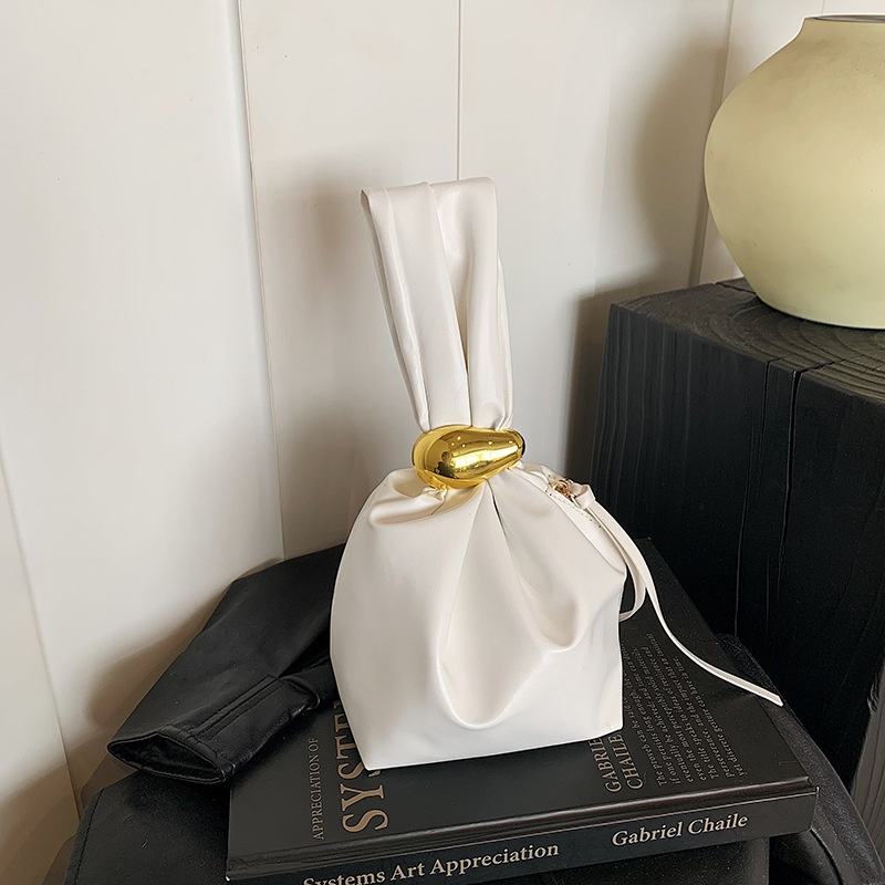White drawstring bag with gold buckle on a book against a neutral background