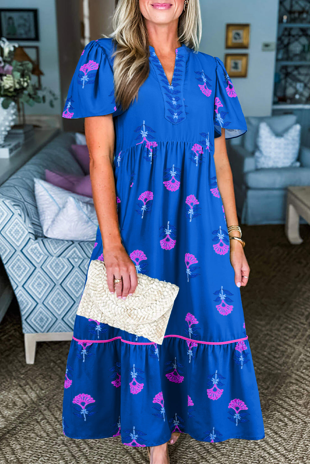 Woman wearing a blue dress with pink floral patterns in a living room setting.