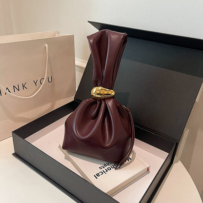 Brown leather handbag with gold buckle on a black box, next to a 'Thank You' bag.