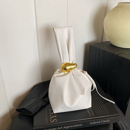 White drawstring bag with gold buckle on a book against a neutral background