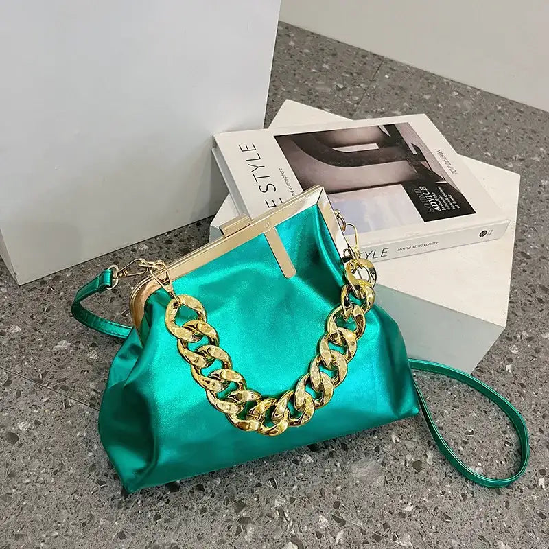 Blue Carauana UNIU Aurora Clutch handbag with gold chain detail on a gray surface