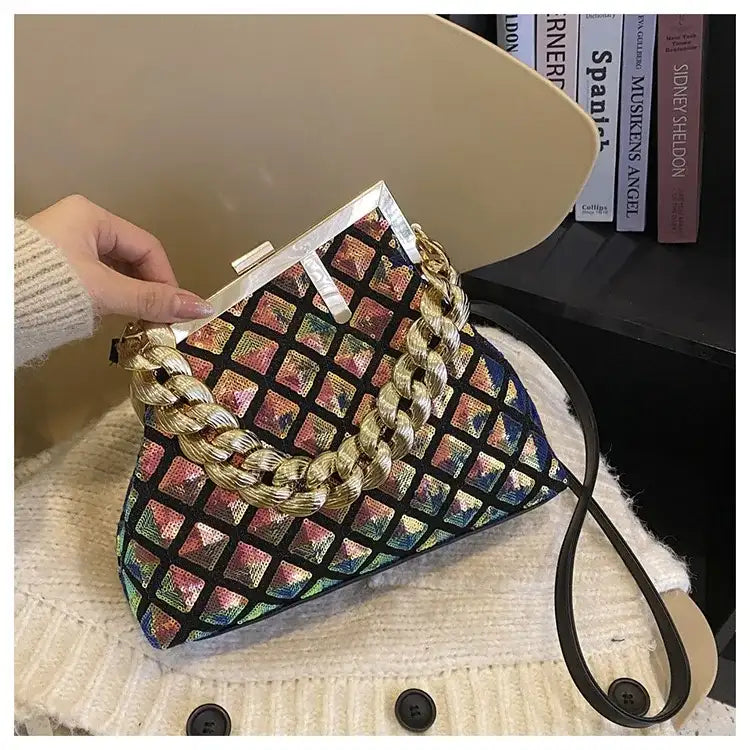 Multicolored patterned handbag with braided handle held by a hand on a textured surface.