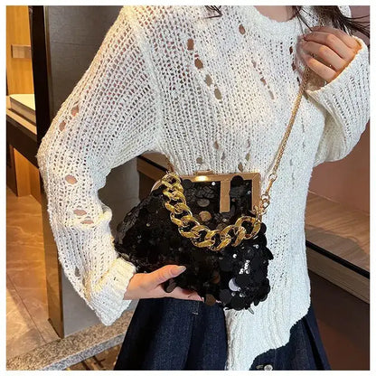 Person wearing a white knit sweater holding a black handbag with gold chain strap.