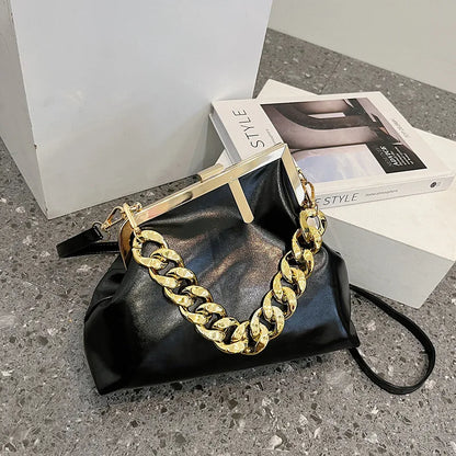 Black Carauana UNIU Aurora Clutch handbag with gold chain detail on a concrete surface