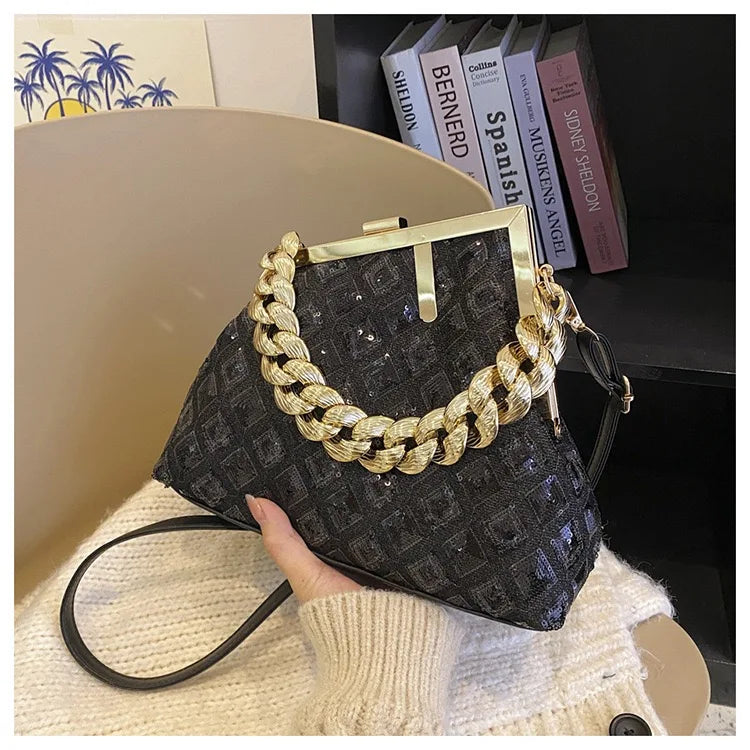 Black handbag with gold chain detail held by a hand on a textured surface.