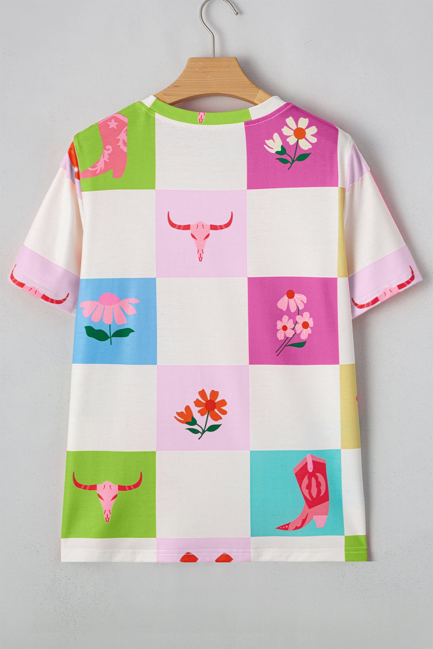 Colorful checkered tee with floral and cowgirl boot patterns on a hanger against a gray background