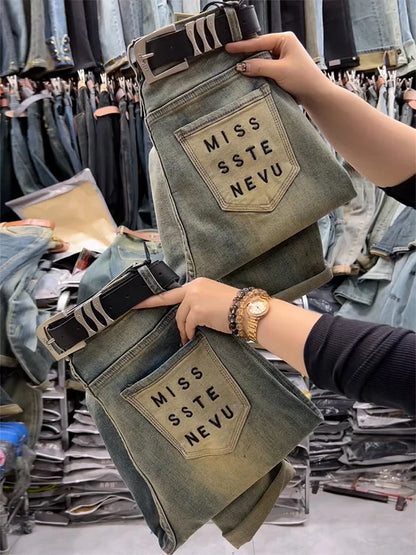 blue jeans with 'MISS SSTE NEVU' patches held by a person in a clothing store.