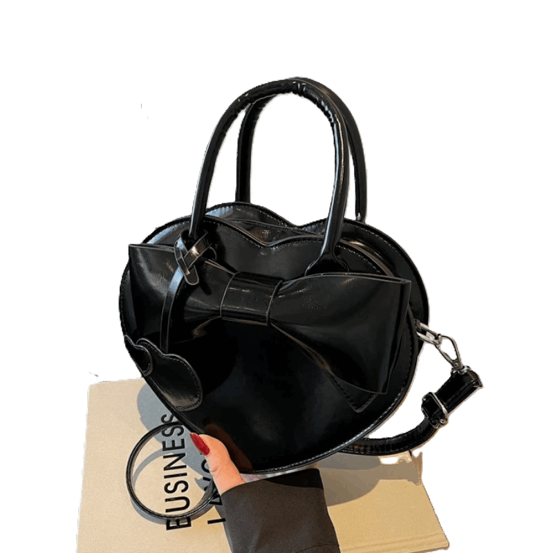 Black handbag with a bow detail held by a hand on a white background