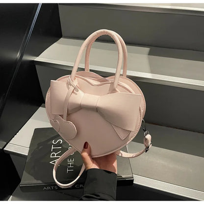 Pink carauana-lovely-shoulder-bag-heart with a large bow held by a person on a gray surface.