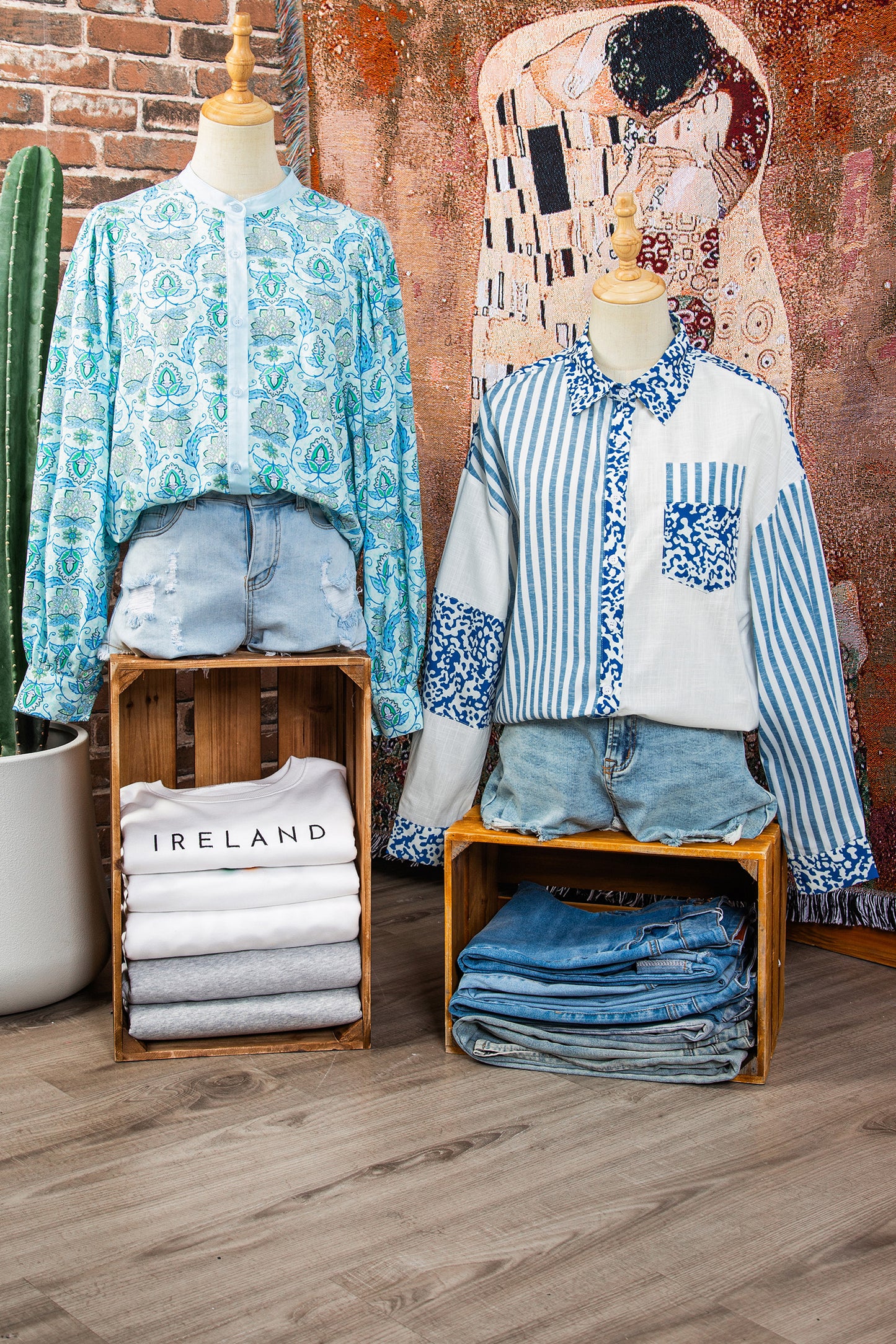 Mannequins wearing patterned shirts and denim shorts with folded clothes underneath against a textured wall.