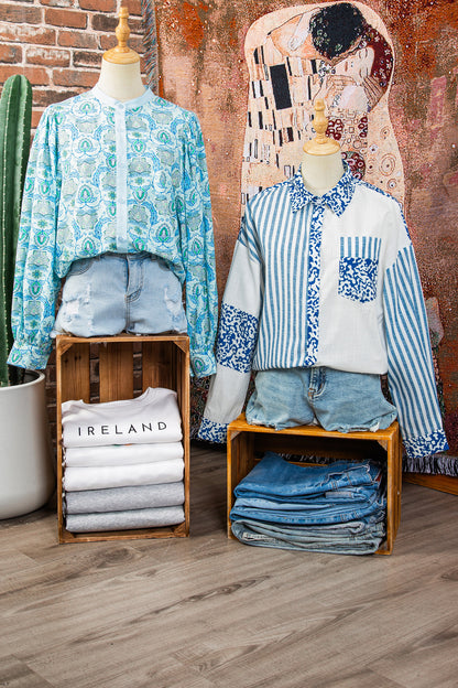 Mannequins wearing patterned shirts and denim shorts with folded clothes underneath against a textured wall.